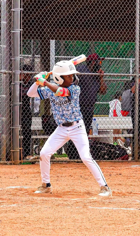 Young baseball player in batting stance at home plate holding bat, ready to swing, with catcher and backstop fence visible.
