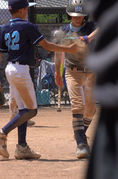 Young baseball players celebrate at home plate during a youth baseball game on a dirt field
